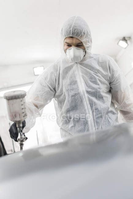 Man in protective suit painting car in auto body shop — Stock Photo