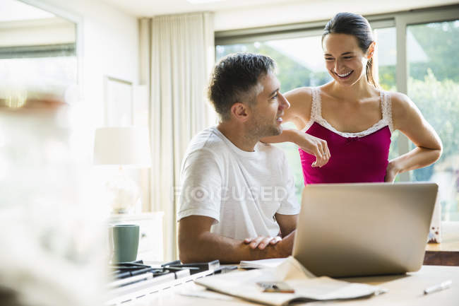 Smiling couple talking at laptop in morning kitchen — Stock Photo