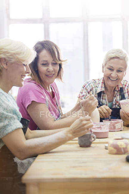 Sonrientes mujeres maduras pintando cerámica en el estudio - foto de stock