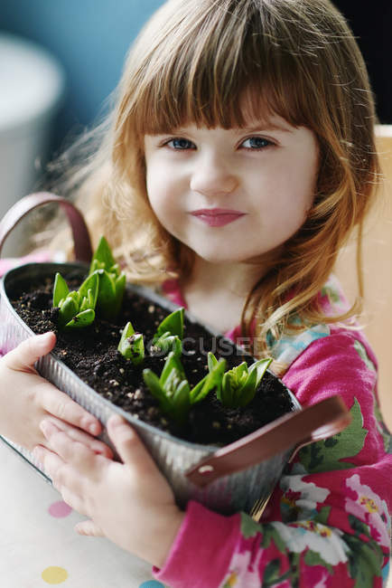 Retrato de cerca de una niña sosteniendo flores brotando en la cesta - foto de stock