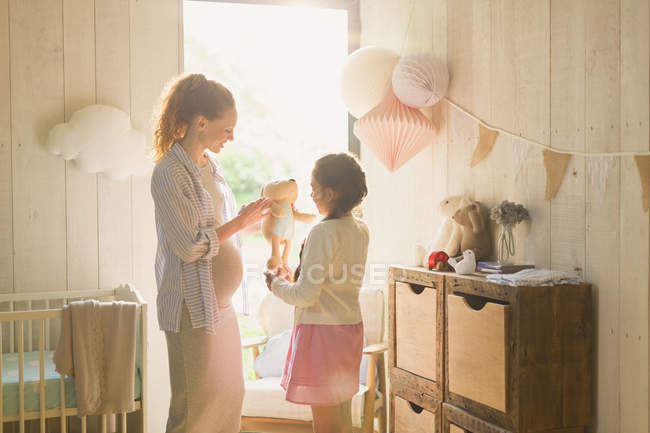 Pregnant mother and daughter looking at stuffed animal in nursery — Stock Photo