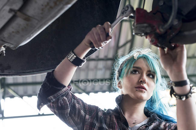 Joven mecánico femenino con pelo azul coche de fijación en taller de reparación de automóviles - foto de stock