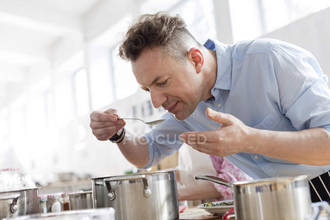 Homem cheirando comida inclinada sobre panela na cozinha aula de culinária — Fotografia de Stock