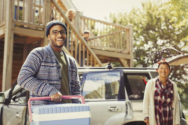 Portrait smiling couple unloading cooler from car outside cabin — Stock Photo