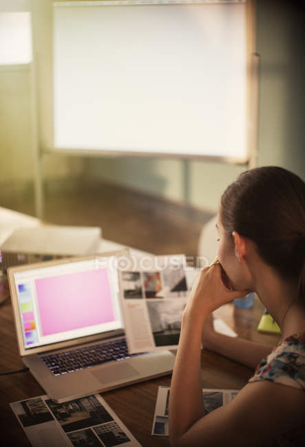 Focused creative businesswoman working at laptop and reviewing photographs — Stock Photo