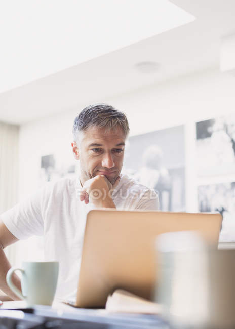 Homme buvant du café et travaillant à l'ordinateur portable dans la cuisine — Photo de stock