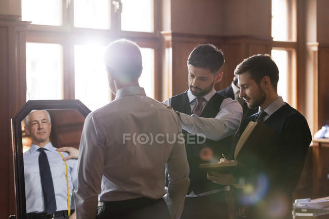 Tailors fitting businessman at mirror in menswear shop — Stock Photo