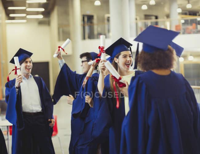 Випускники коледжу в шапці і сукні тримають дипломи — стокове фото