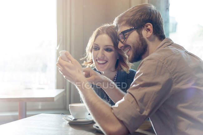 Пара, использующая мобильный телефон в солнечном кафе — стоковое фото