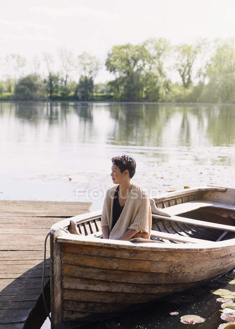 Femme sereine assise en canot au quai ensoleillé au bord du lac — Photo de stock