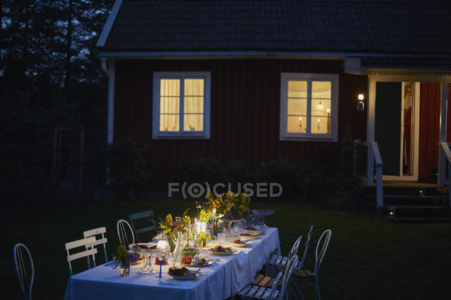 Cena de fiesta en el jardín a la luz de las velas casa iluminada exterior por la noche - foto de stock