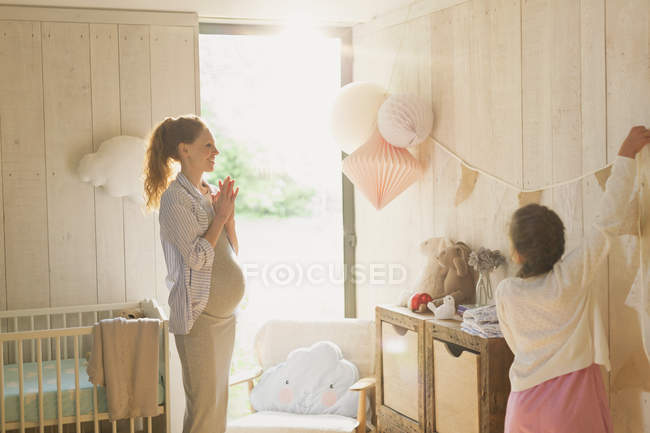 Pregnant mother and daughter decorating sunny nursery — Stock Photo