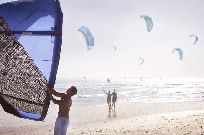 Homem preparando kiteboarding pipa na praia ensolarada — Fotografia de Stock