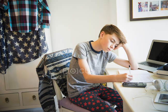 Скучный мальчик делает домашнее задание по математике в спальне — стоковое фото