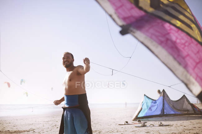 Sonriente hombre tirando kitesurf cometa en la playa soleada - foto de stock