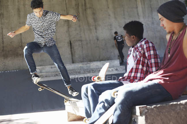 Amigos viendo adolescente haciendo acrobacias en skate park - foto de stock