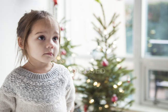 Wide-eyed girl looking up in front of Christmas tree — Stock Photo