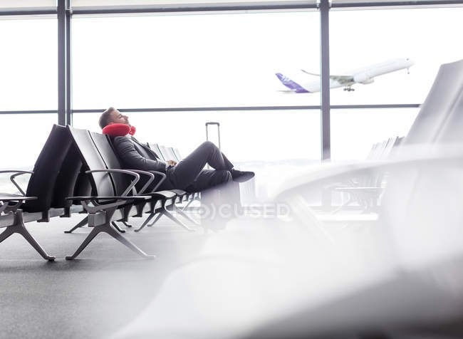 Бизнесмен отдыхает с подушкой на шее в зоне вылета из аэропорта — стоковое фото