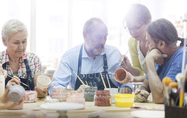 Enseignant guidant des étudiants matures peignant des poteries en studio — Photo de stock