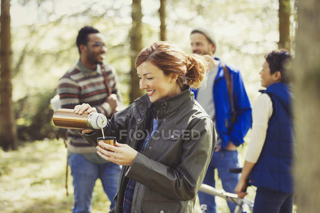 Mujer sonriente senderismo verter café de recipiente de bebida aislada en los bosques - foto de stock