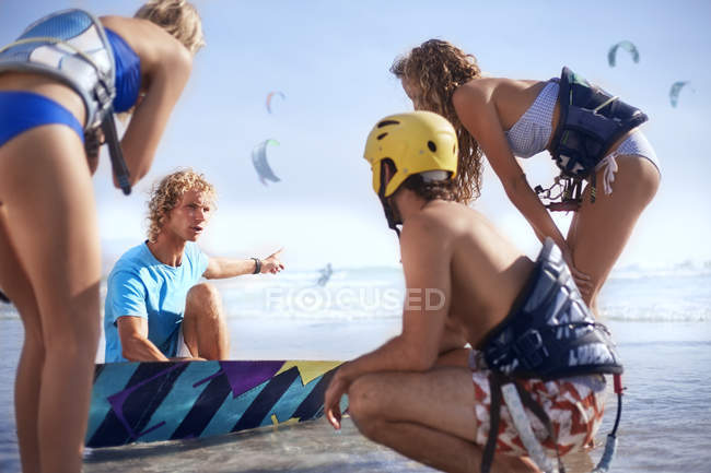 Homem ensinando amigos kiteboarding na praia ensolarada — Fotografia de Stock