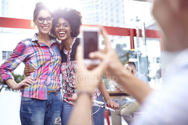 Hombre fotografiando mujeres sonrientes con el teléfono de la cámara - foto de stock