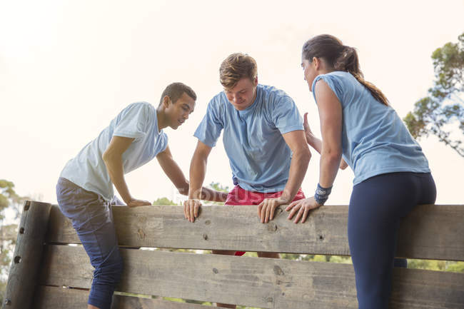 Партнеры по команде помогают человеку перелезть через стену на полосе препятствий учебного лагеря — стоковое фото
