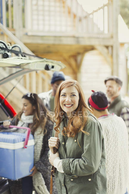 Portrait femme souriante avec des amis déchargement refroidisseur de l'arrière de la voiture — Photo de stock