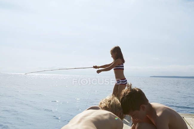 Girl in bikini fishing off sunny dock — Stock Photo