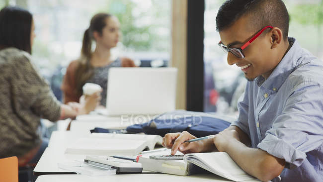 Männlicher College-Student macht Mathe-Hausaufgaben mit Lehrbuch und Taschenrechner — Stockfoto
