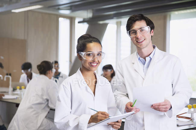 Портрет впевнених студентів коледжу в лабораторних пальтах в науково-лабораторному класі — стокове фото