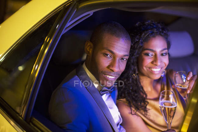 Well-dressed couple drinking champagne inside limousine — Stock Photo