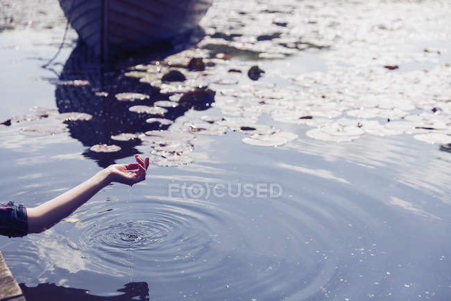 Acqua gocciolante dalla mano della donna al lago soleggiato con i cuscinetti del giglio — Foto stock