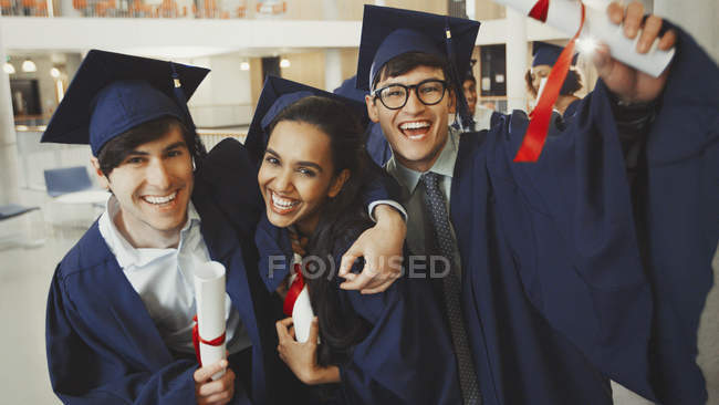 Portrait diplômés enthousiastes du collège en casquette et robe avec des diplômes — Photo de stock