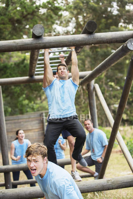 Determined man crossing monkey bars on boot camp obstacle course — Stock Photo