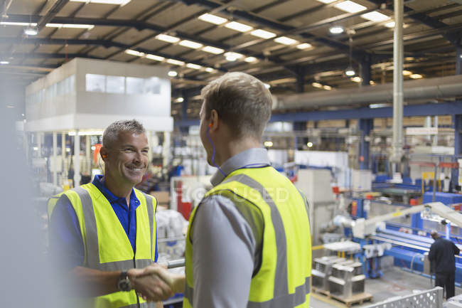 Smiling supervisor and worker handshaking in steel factory — Stock Photo