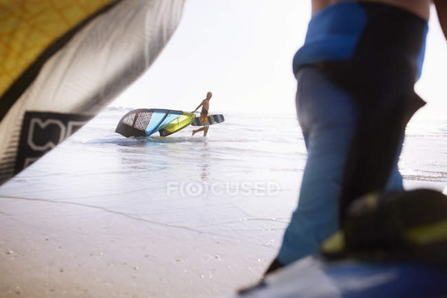 Man pulling kiteboarding equipment into ocean surf — Stock Photo