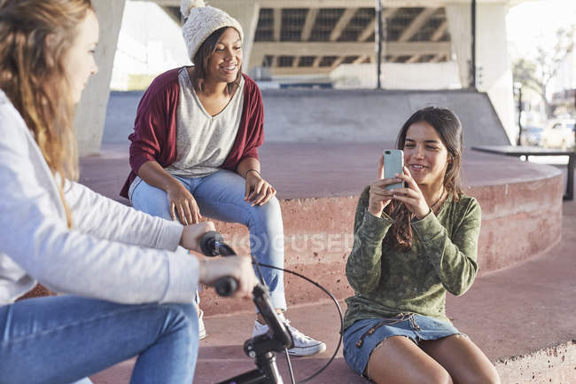 Teenage girls using camera phone at skate park — Stock Photo