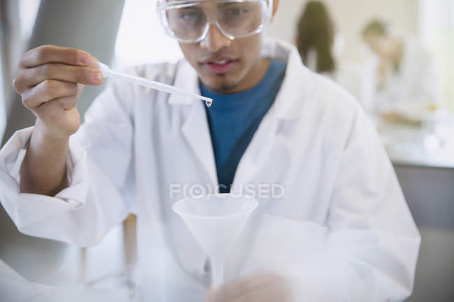 Estudiante universitario masculino realizando experimento científico usando pipeta en el aula de laboratorio de ciencias - foto de stock