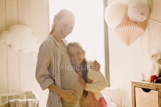 Porträt lachende schwangere Mutter und Tochter im sonnigen Kinderzimmer — Stockfoto