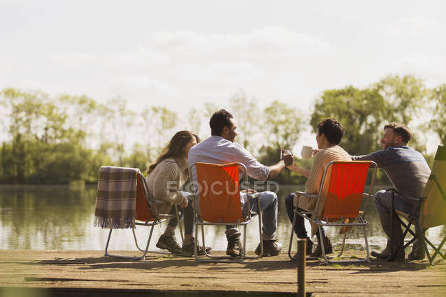 Des amis grillent des tasses à café au quai ensoleillé au bord du lac — Photo de stock