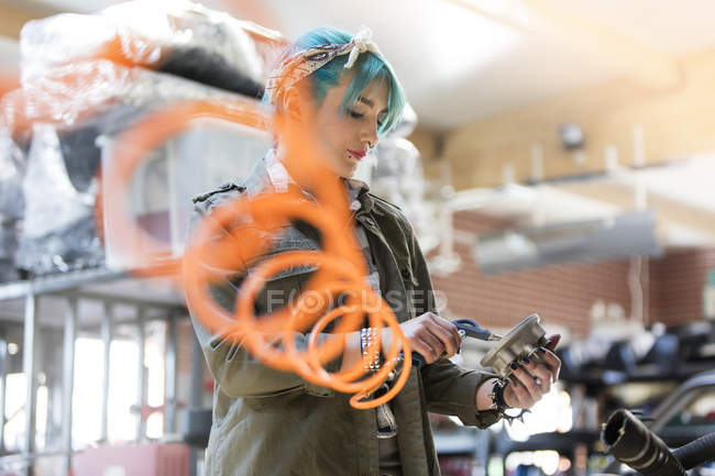 Молода жінка-механік з блакитним волоссям використовує обладнання в авторемонтному магазині — стокове фото