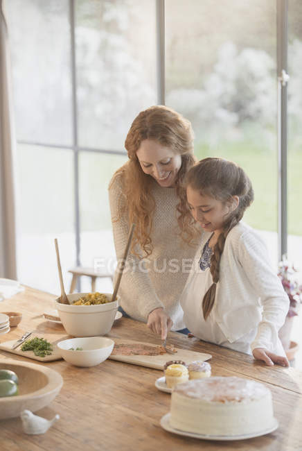 Madre e hija embarazadas preparando comida en la mesa de comedor - foto de stock