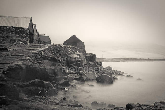 Black and white image of houses on cliff over water — Stock Photo