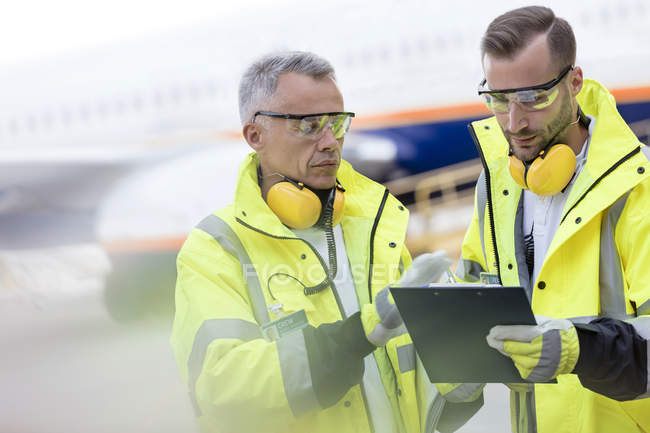 Controladores de tráfico aéreo con portapapeles hablando en asfalto del aeropuerto - foto de stock