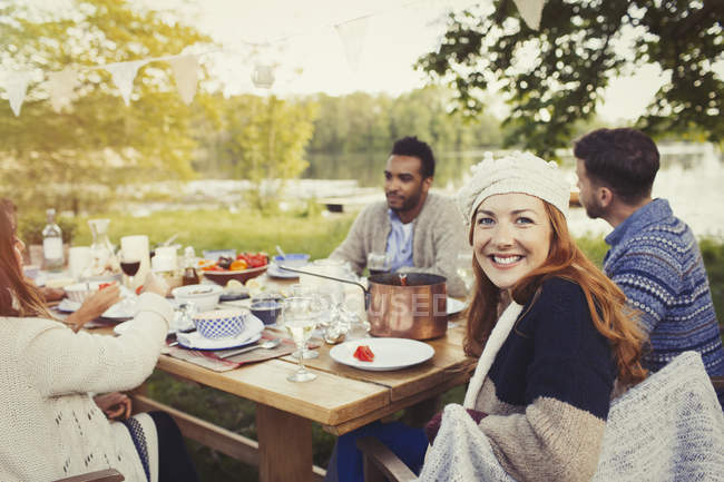 Retrato sorridente mulher desfrutando de almoço na mesa do pátio à beira do lago — Fotografia de Stock