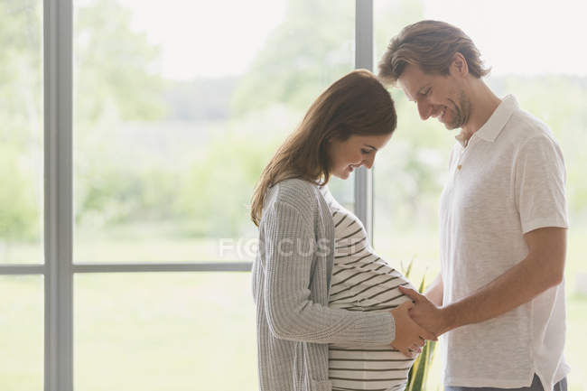Cariñosa pareja embarazada tocando el estómago - foto de stock