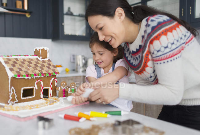 Mother and daughter decorating gingerbread house — Stock Photo