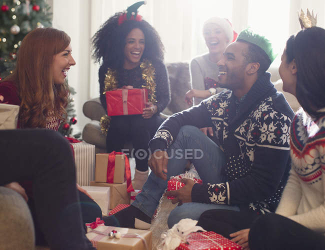 Amigos riéndose abriendo regalos de Navidad en la sala de estar - foto de stock