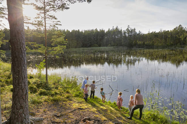 Grandparents and grandchildren fishing at sunny lakeside in woods — Stock Photo